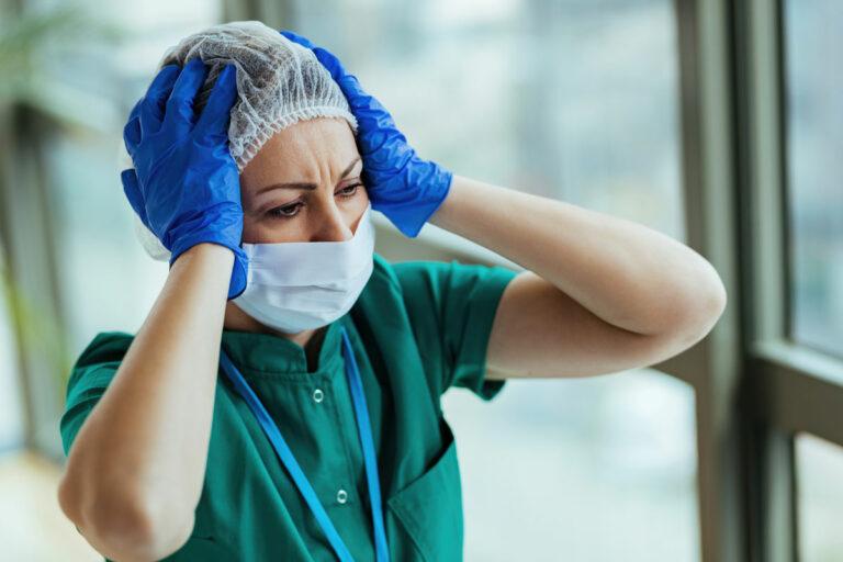 340302b distraught nurse wearing protective workwear while holding her head pain medical clinic - Genauso falsch wie überall - Zeitarbeit - Zeitarbeit